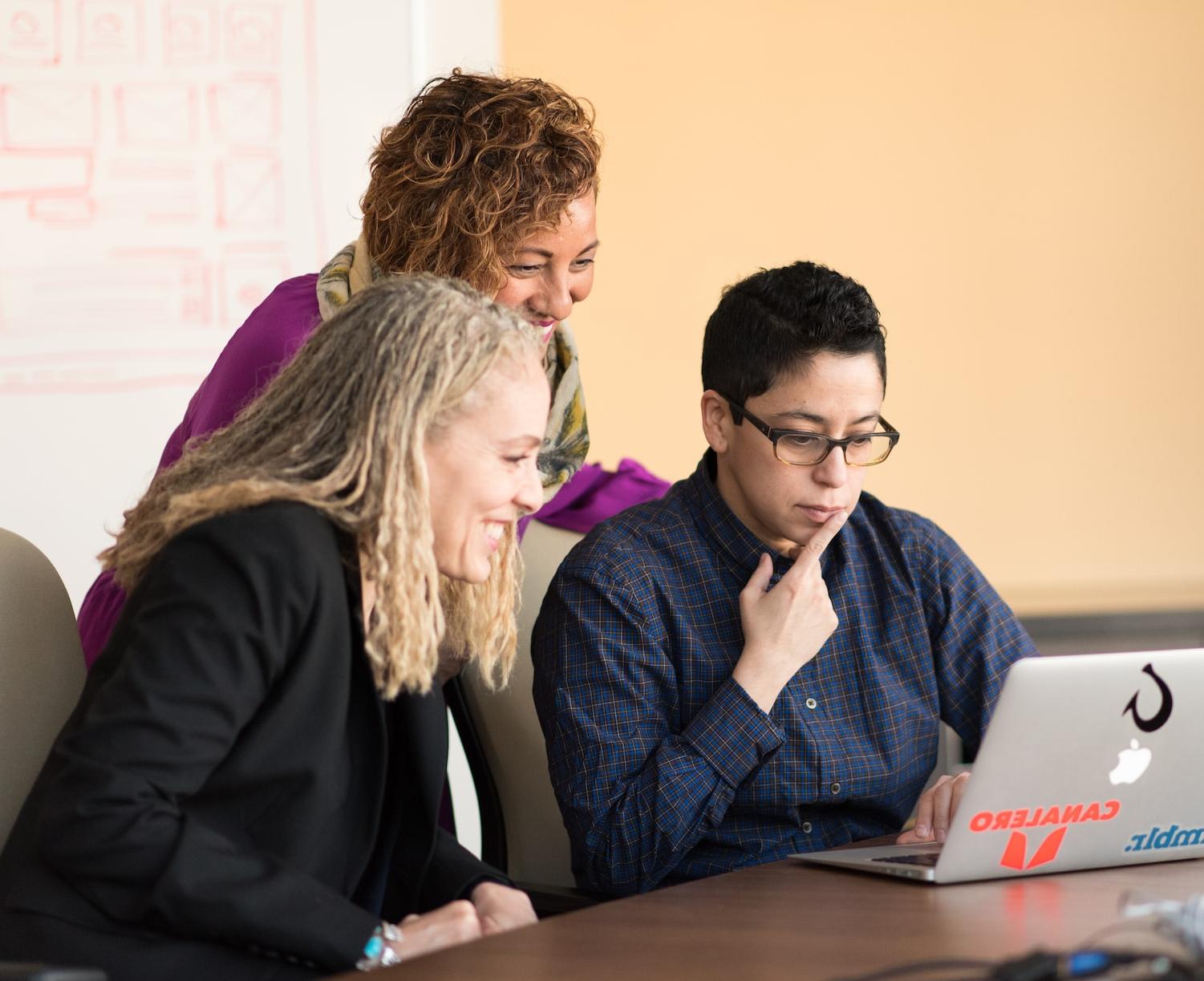 three women beside table looking at MacBook